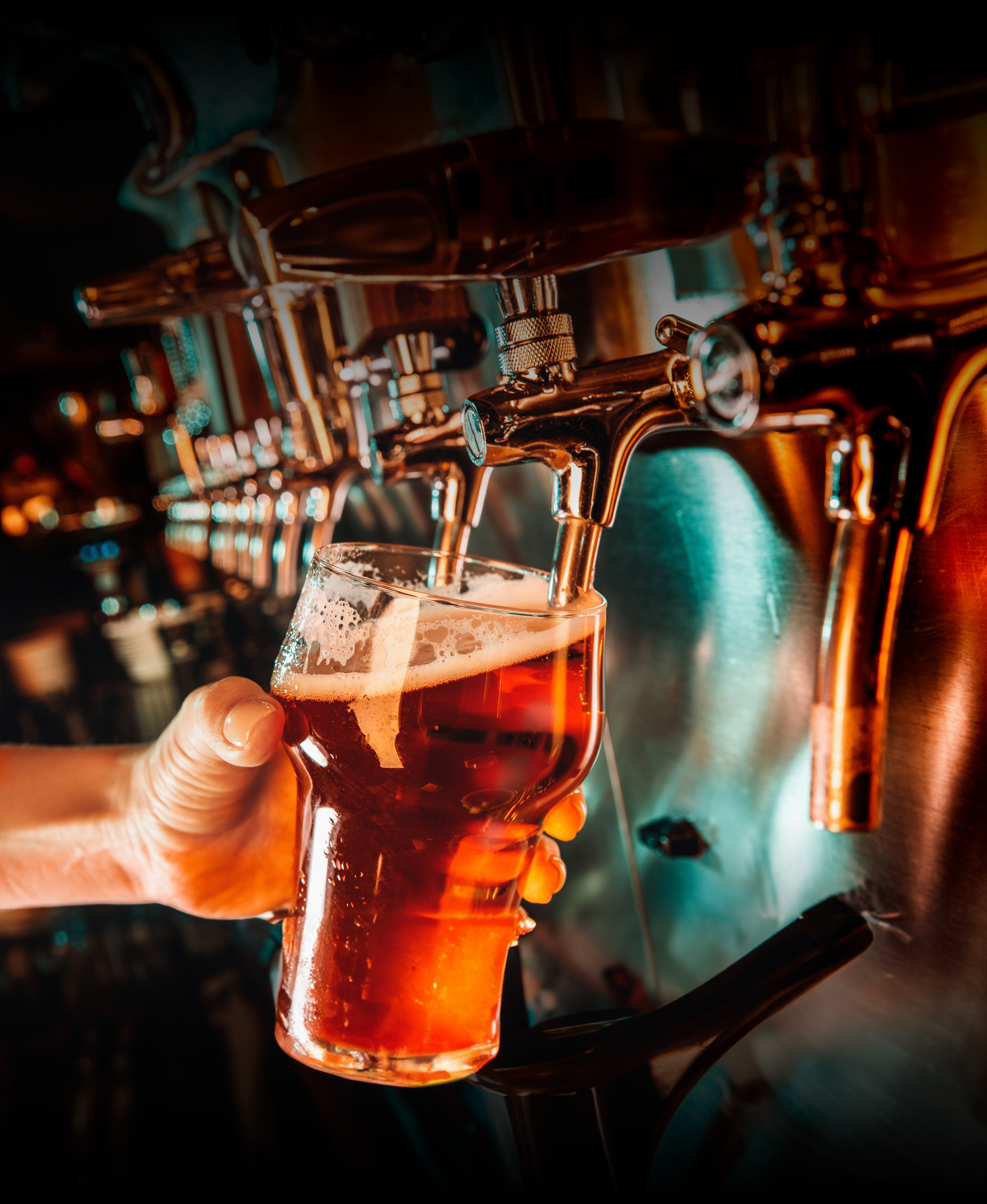 Ręka barmana trzymająca kufel napełniany piwem z nalewaka.